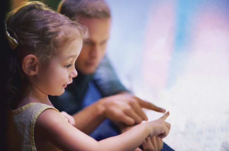 Young girl with father looking through aquarium glass